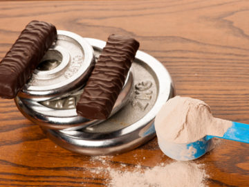 55159312 - whey protein powder in measuring scoop, protein bar, meter tape and dumbbell on wooden background.